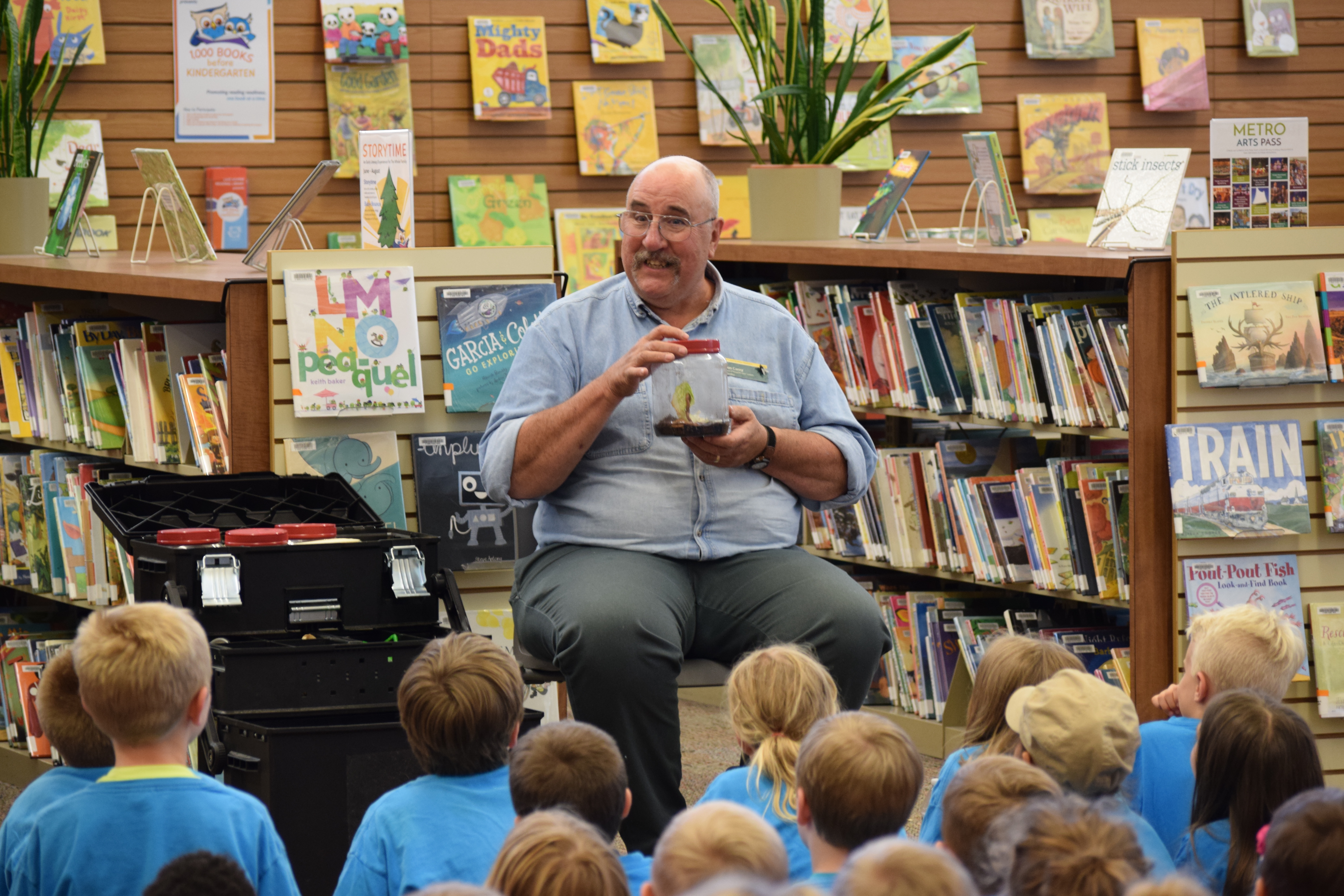Man With A Plant In A Jar Talking To Children